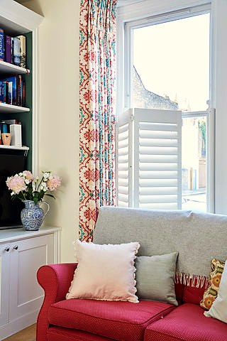 part of a room with a sofa and behind a window with shutters and curtains