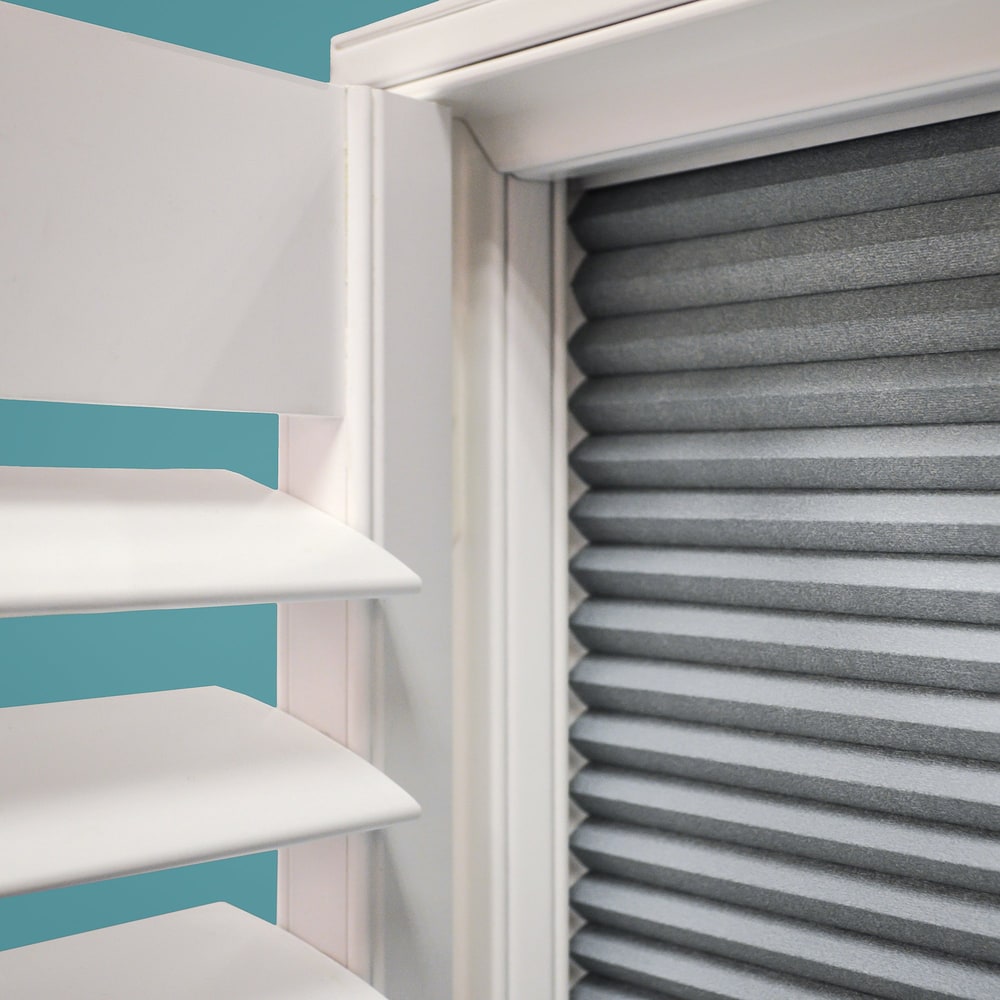 Close view of a grey room-darkening blind fitted behind white plantation shutters