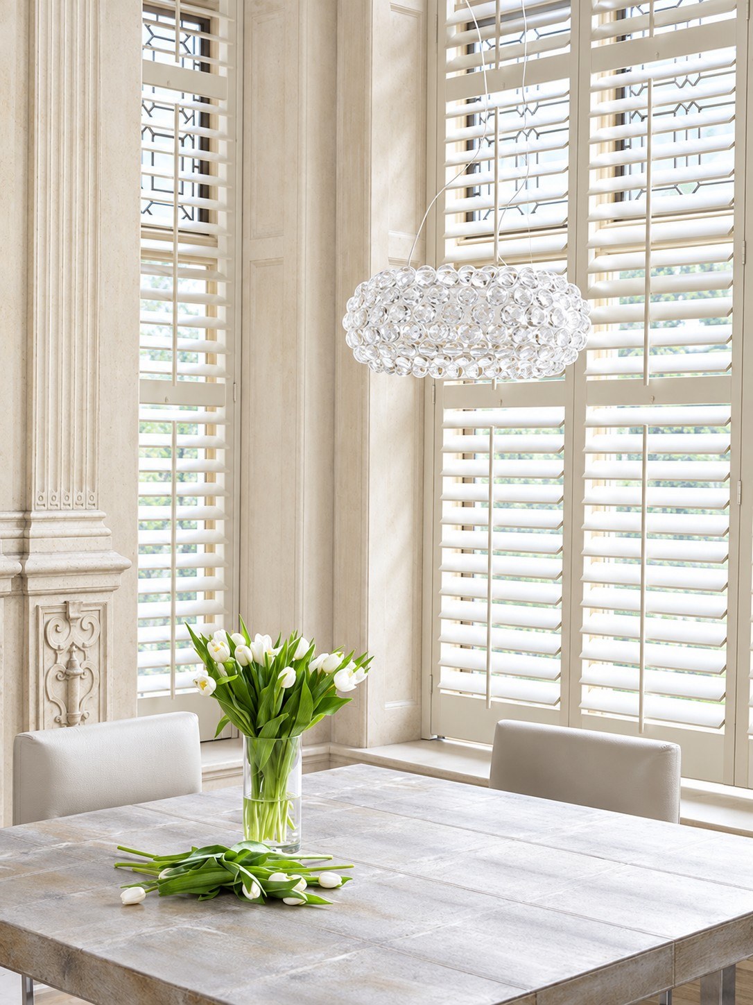 White full height plantation shutters in a tall dining room window, tulips on the table