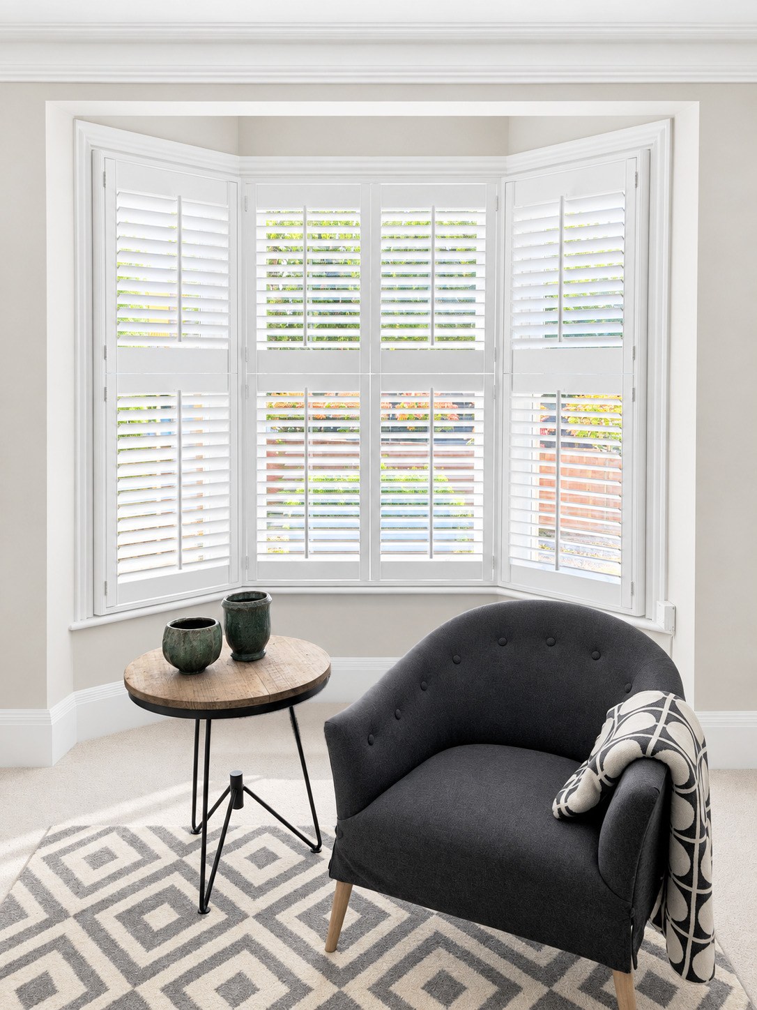 White made-to-measure shutters fitted around a bay window beside an armchair