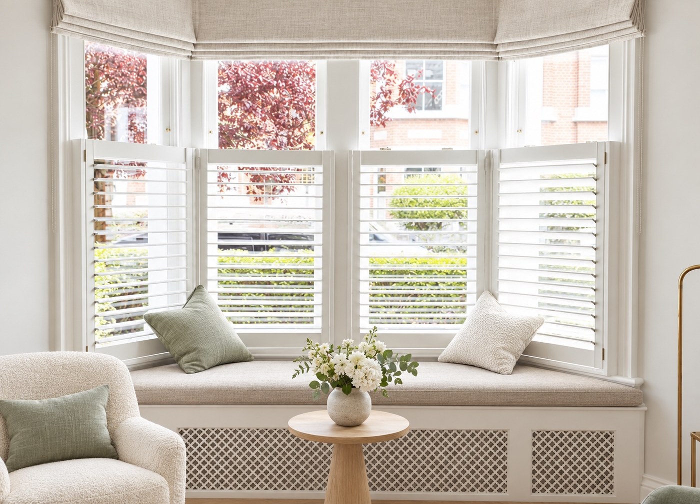 White café style plantation shutters fitted across a bay window with a cushioned window seat