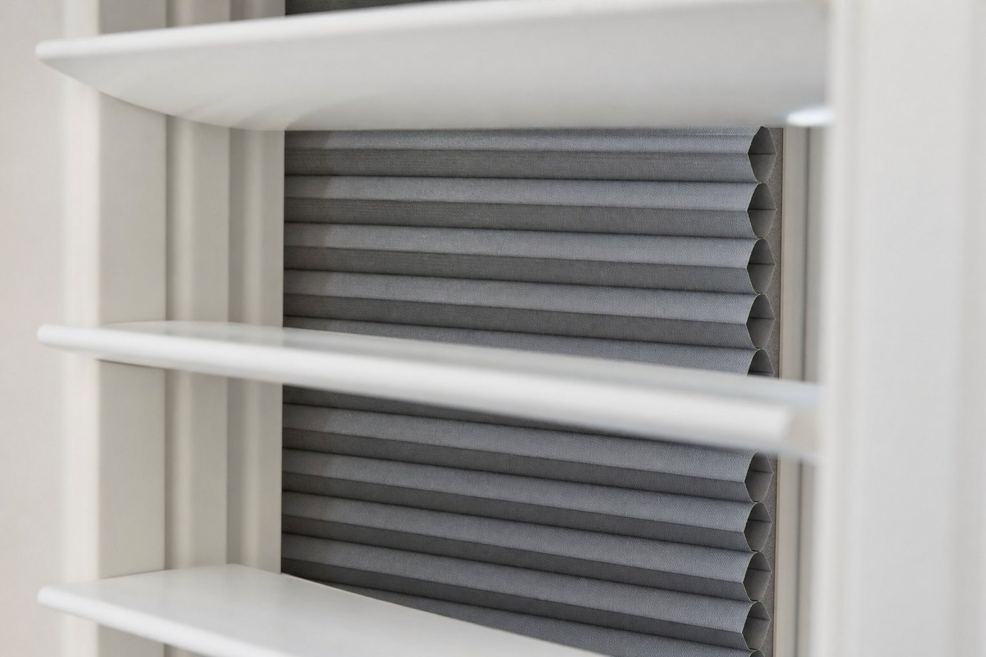 Room darkening blind sitting in its channel behind open shutter louvres