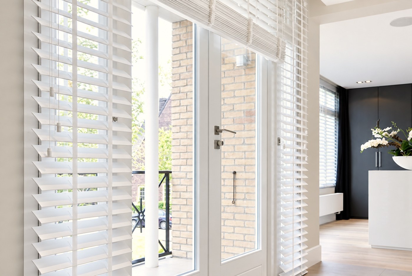 White wooden Venetian blinds on tall windows and a glazed door in a bright modern home