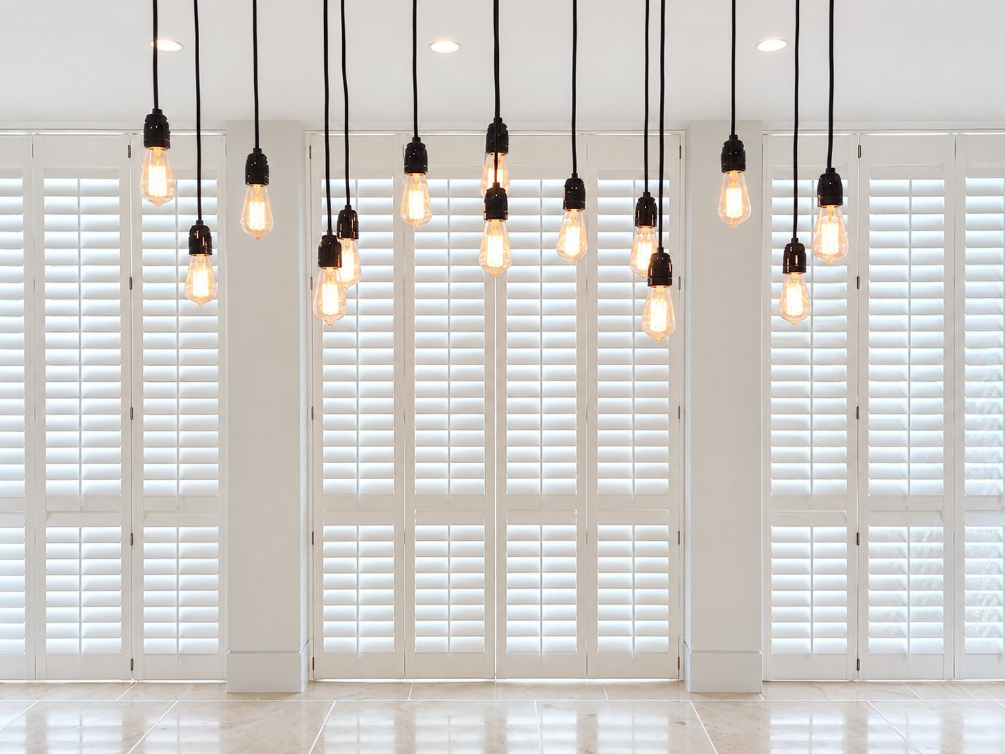 Cream full-height shutters in a dining room with pendant lights