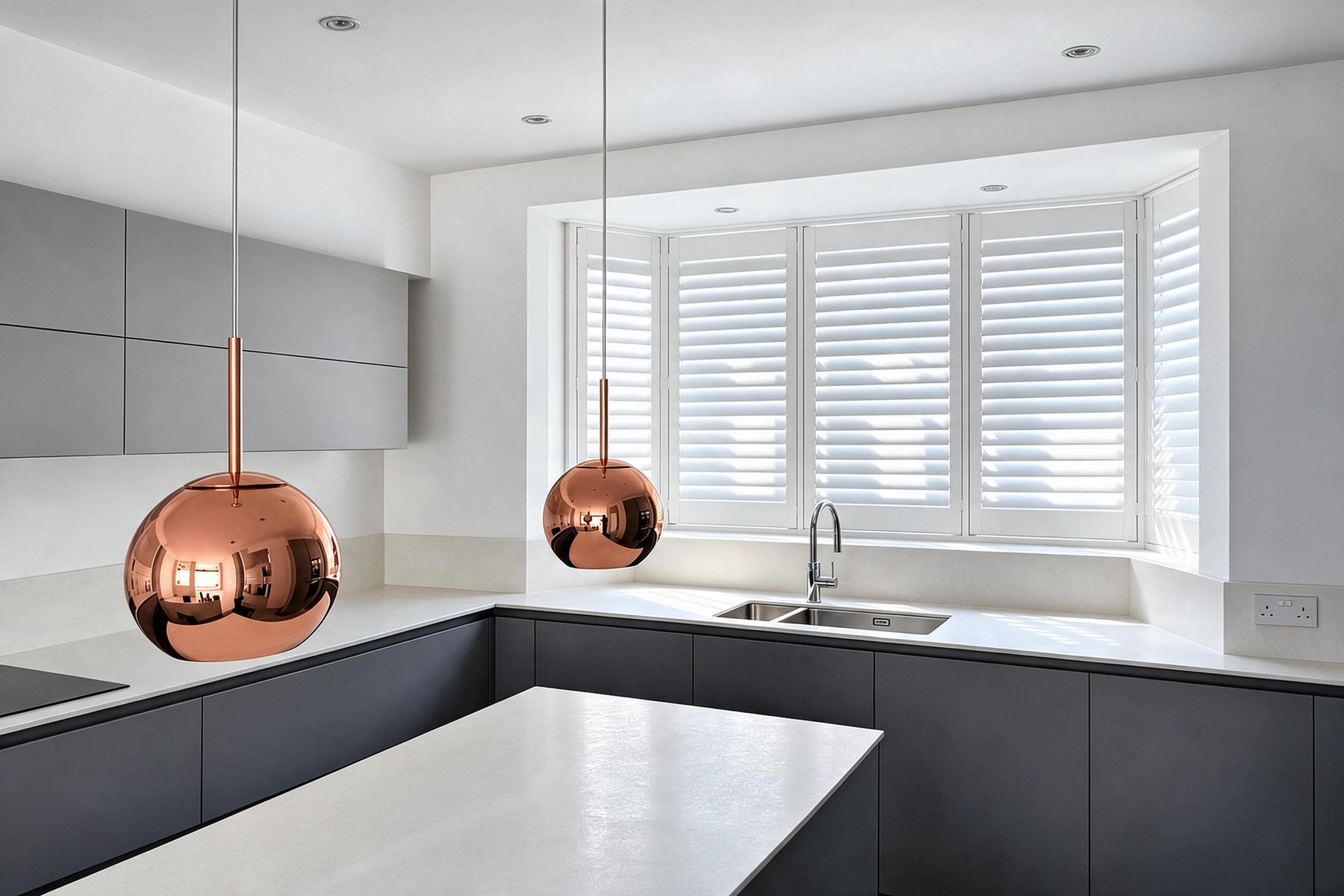 White plantation shutters fitted across a kitchen bay window, with copper pendant lights over the island