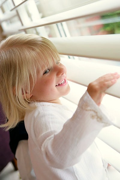 child looking out a window through window shutters