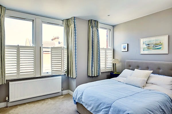 bedroom with large windows with half shutters and white curtains. Picture taken in a flat in Shepherd