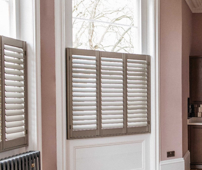Café Style wooden shutters fitted to a tall kitchen window in a room with pink walls and a radiator