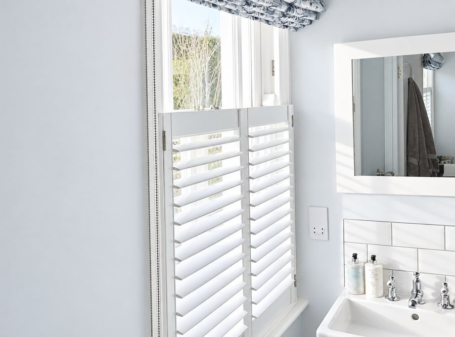White café style shutters and a roman blind in a bathroom