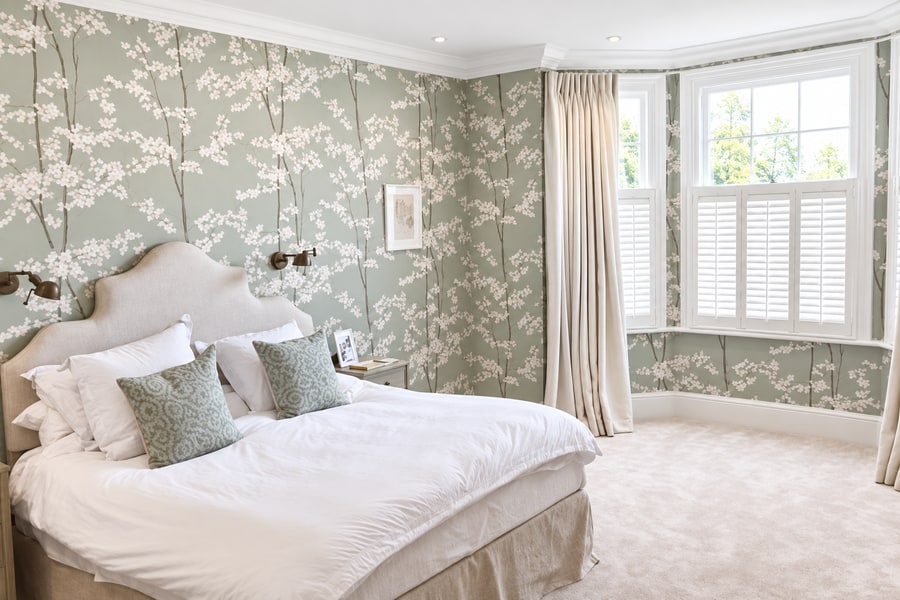 Café style shutters in a bay window in a wallpapered bedroom