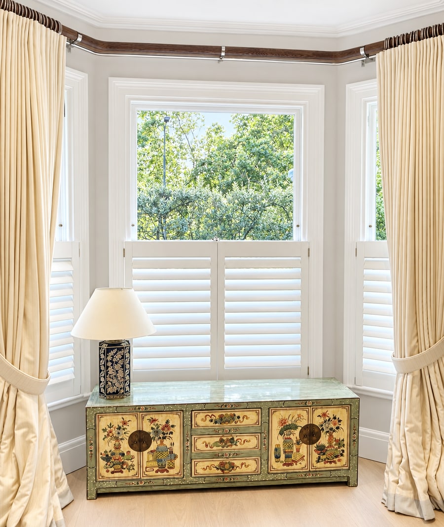 Café style shutters in a bay window with gold curtains