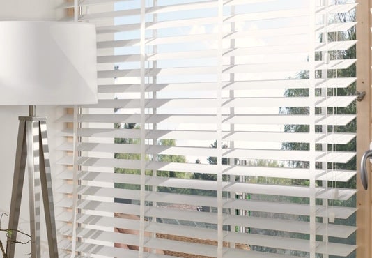 White wooden Venetian blind beside a floor lamp in a bright living room